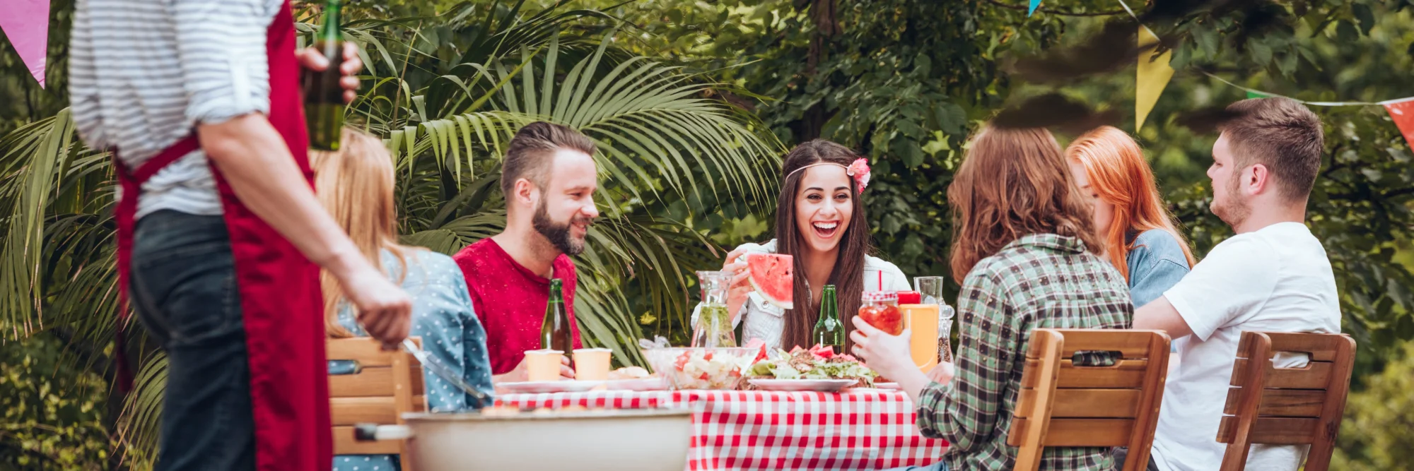 Friends gathered around an outdoor table with food and drinks at a garden party