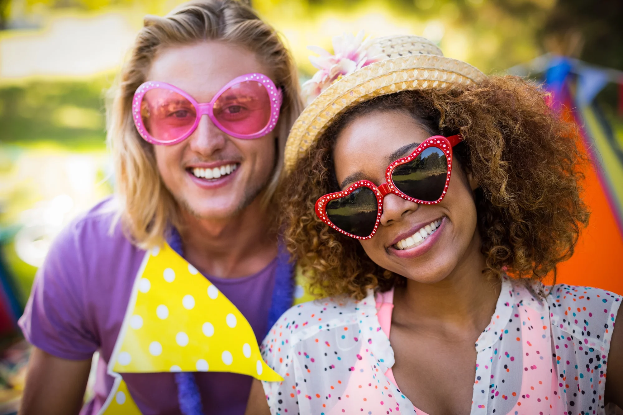 Two friends in retro heart and round sunglasses laughing at an outdoor garden party